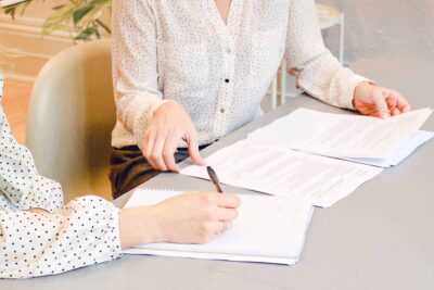 Todo sobre el certificado de conformidad para arrendamiento 1 woman signing on white printer paper beside woman about to touch the documents